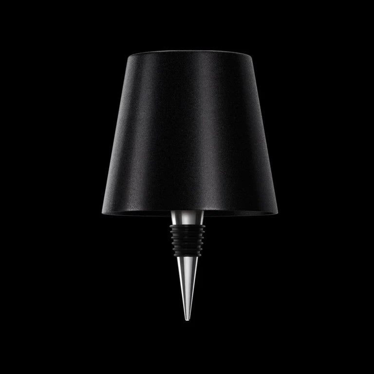 AMBIENTIFY Bottle wireless LED lamp fitted onto a wine bottle, placed on an outdoor garden table surrounded by natural greenery. Soft warm ambient glow, touch-dimmable in 3 levels, USB-C rechargeable table lamp for home décor.