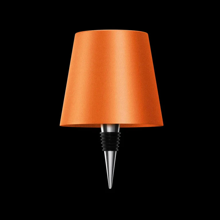 AMBIENTIFY Bottle wireless LED lamp fitted onto a wine bottle, placed on an outdoor garden table surrounded by natural greenery. Soft warm ambient glow, touch-dimmable in 3 levels, USB-C rechargeable table lamp for home décor.