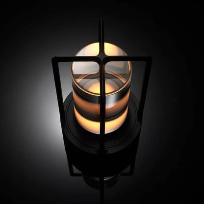 AMBIENTIFY Retro cordless retro table lantern lamp casting a warm amber glow, placed on a wooden tray. Slender aluminium frame with cylindrical acrylic glass shade. Atmospheric home décor lighting for bedroom, living room or outdoor use.