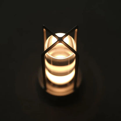 AMBIENTIFY Retro cordless retro table lantern lamp casting a warm amber glow, placed on a wooden tray. Slender aluminium frame with cylindrical acrylic glass shade. Atmospheric home décor lighting for bedroom, living room or outdoor use.