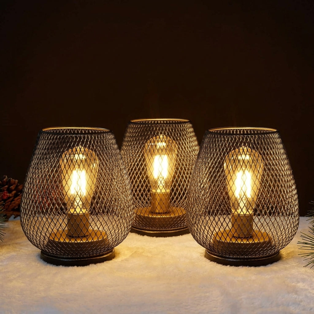 Ambientify Vira cordless metal mesh cage table lamp with a warm Edison-style bulb glowing through a diamond-pattern shade, placed on a wooden surface beside dried flowers and stacked books in a contemporary home interior.