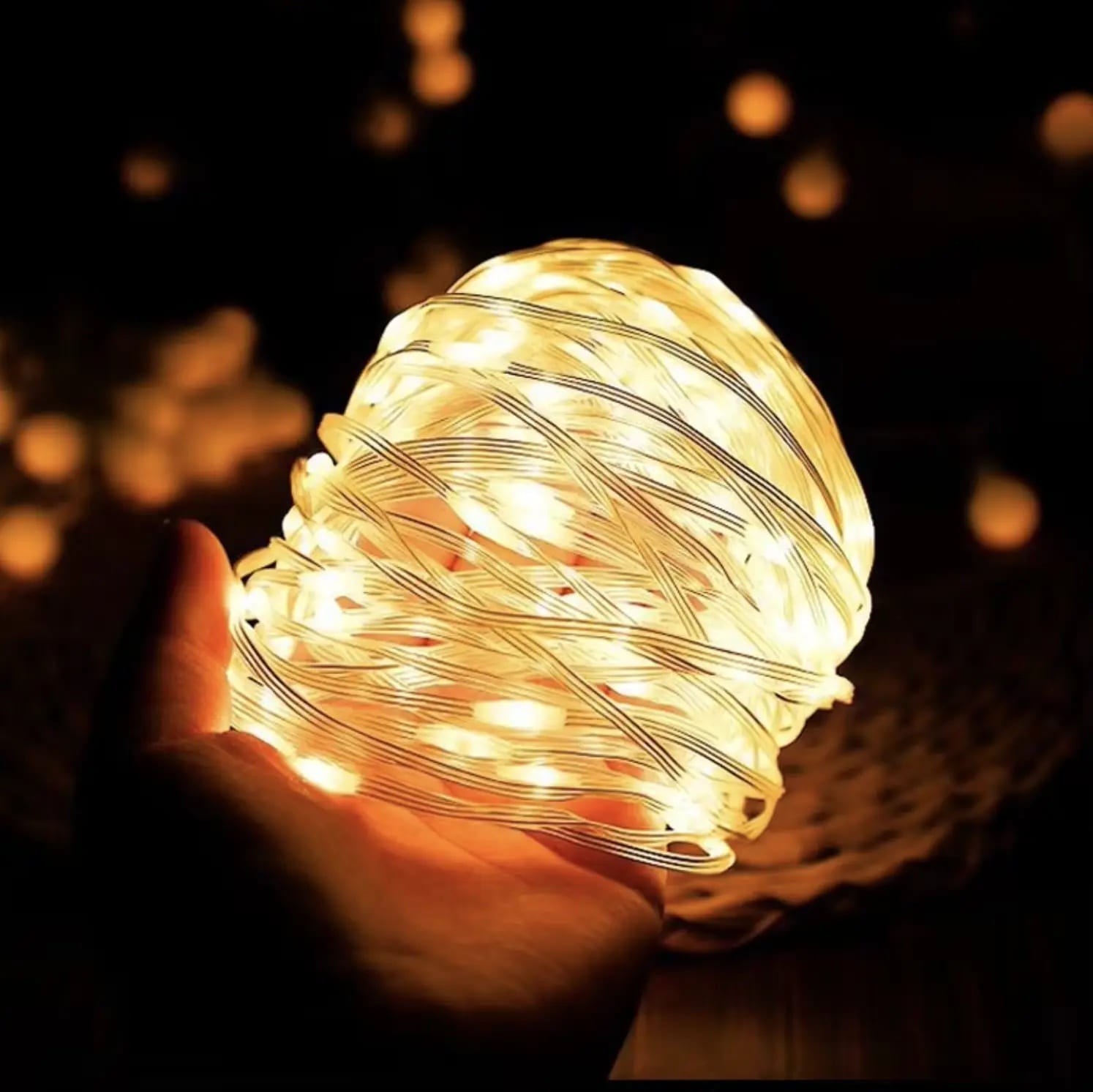 Campify String fairy light reel held in hand at night, showing warm amber LED string lights extended across dark outdoor ground, compact hub glowing with blue charge indicator, IP67 waterproof camping and home fairy lights.
