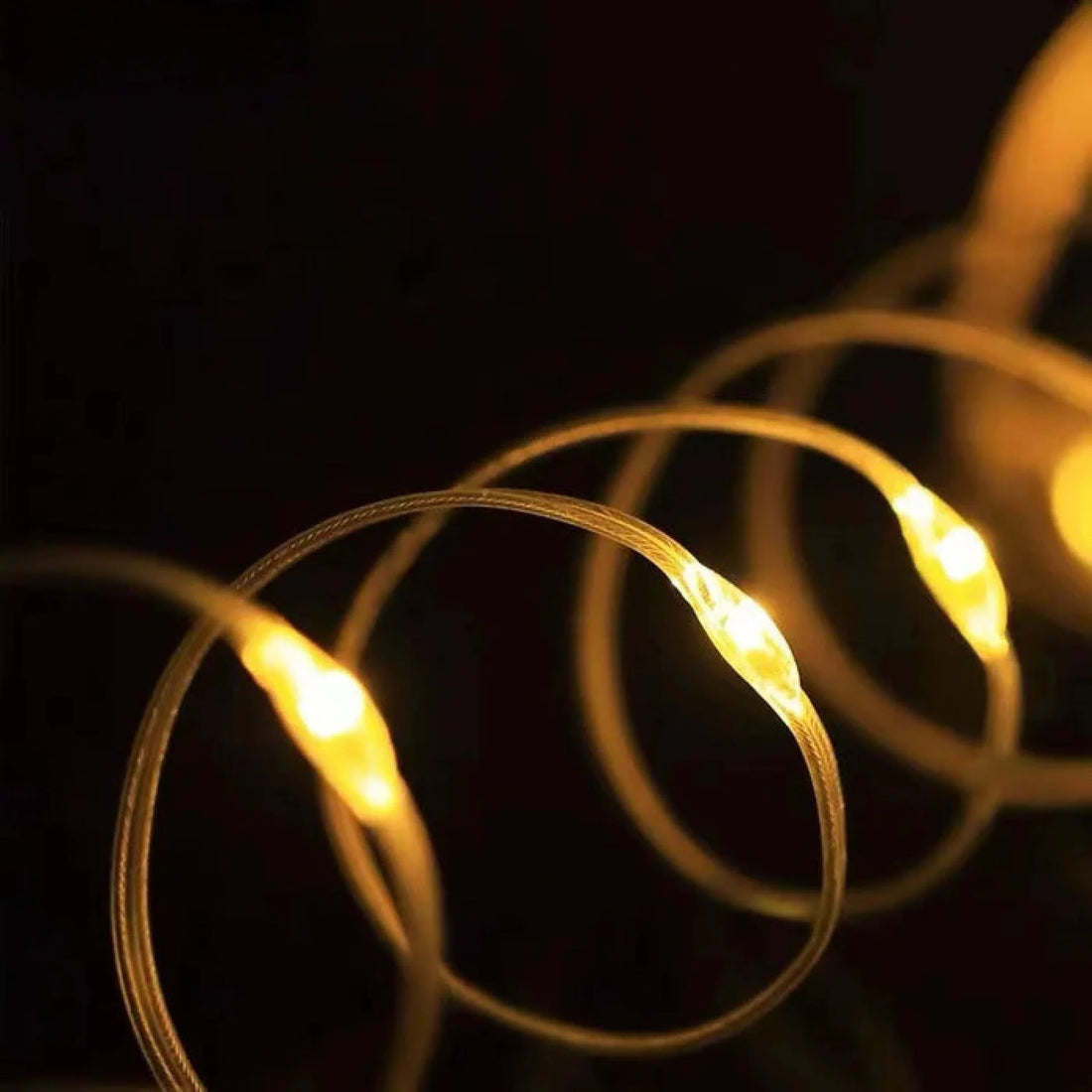 Campify String fairy light reel held in hand at night, showing warm amber LED string lights extended across dark outdoor ground, compact hub glowing with blue charge indicator, IP67 waterproof camping and home fairy lights.
