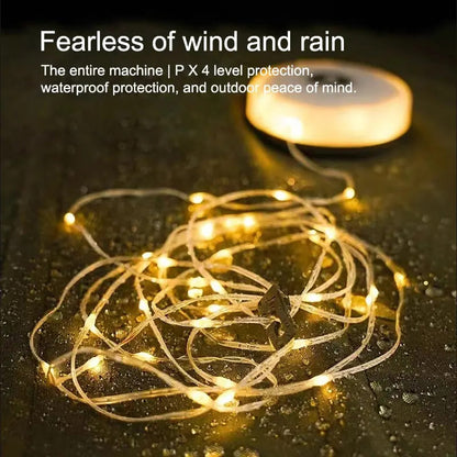 Campify String fairy light reel held in hand at night, showing warm amber LED string lights extended across dark outdoor ground, compact hub glowing with blue charge indicator, IP67 waterproof camping and home fairy lights.