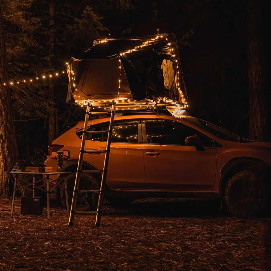 Campify String fairy light reel held in hand at night, showing warm amber LED string lights extended across dark outdoor ground, compact hub glowing with blue charge indicator, IP67 waterproof camping and home fairy lights.