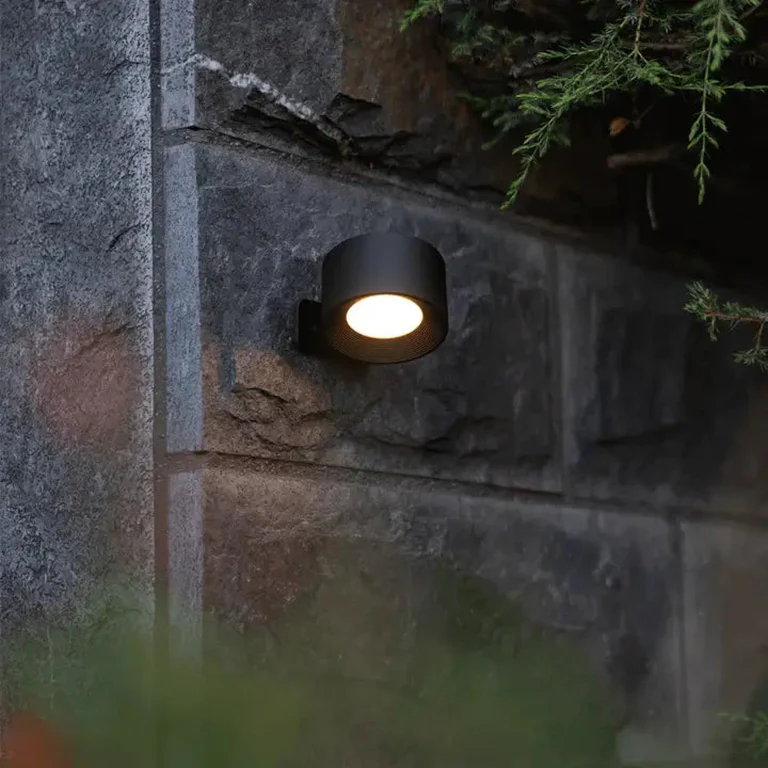 LUNIFY 360 wireless rechargeable LED spotlight with a circular concentric ring surround, mounted on a wall and casting warm amber light in a minimal interior — equally suited as a freestanding spotlight on a shelf or side table.