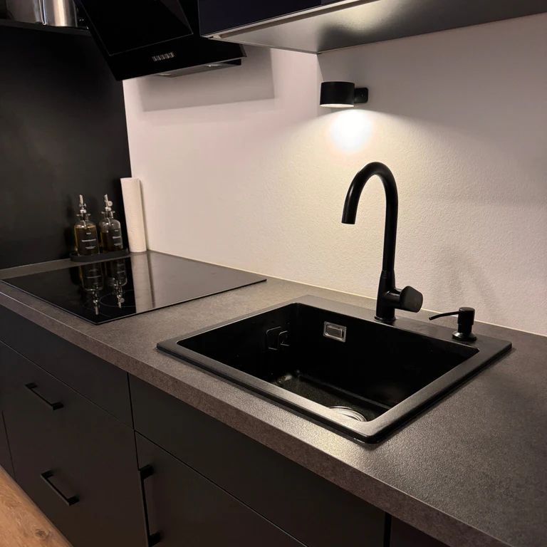 LUNIFY 360 wireless rechargeable LED spotlight with a circular concentric ring surround, mounted on a wall and casting warm amber light in a minimal interior — equally suited as a freestanding spotlight on a shelf or side table.
