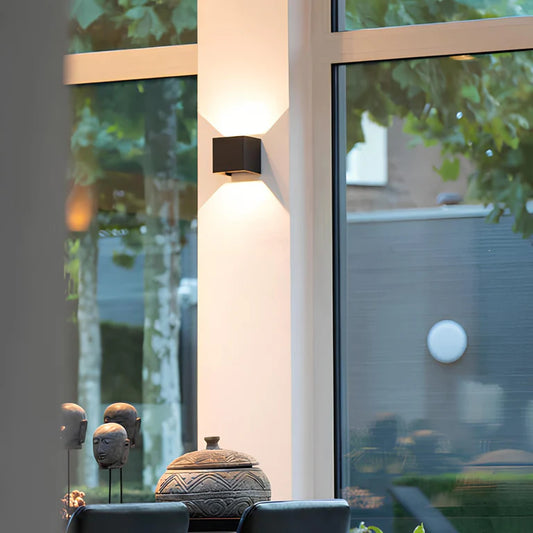 LUNIFY Boca compact aluminium wall light mounted on a slatted wood wall, casting a warm 2700K up-and-down glow. Wireless rechargeable LED wall lamp with motion sensor and magnetic mounting for wire-free indoor installation.