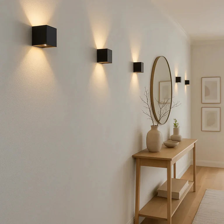 LUNIFY Boca compact aluminium wall light mounted on a slatted wood wall, casting a warm 2700K up-and-down glow. Wireless rechargeable LED wall lamp with motion sensor and magnetic mounting for wire-free indoor installation.
