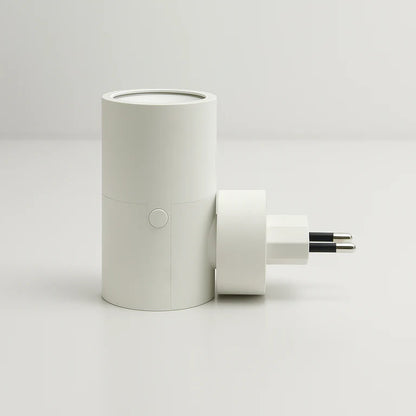 PLUGIFY One plug-in wall light in matte finish mounted in a bedroom wall socket, casting warm ambient light onto a wooden bedside table with a remote control and ceramic mug beside it.