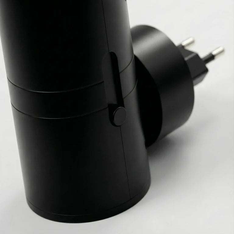PLUGIFY One plug-in wall light in matte finish mounted in a bedroom wall socket, casting warm ambient light onto a wooden bedside table with a remote control and ceramic mug beside it.