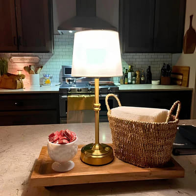 AMBIENTIFY Classic cordless table lamp with fabric shade and iron stem, casting warm ambient light on a bedside table. Three brightness settings and up to 40 hours battery life. Suitable for bedroom, living room and home office.