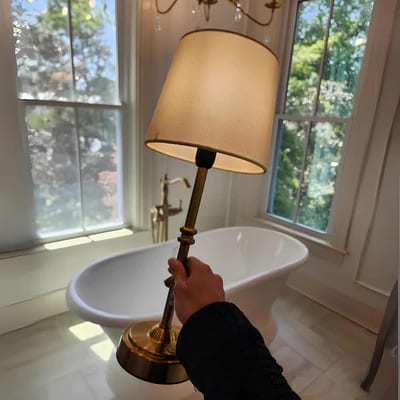 AMBIENTIFY Classic cordless table lamp with fabric shade and iron stem, casting warm ambient light on a bedside table. Three brightness settings and up to 40 hours battery life. Suitable for bedroom, living room and home office.