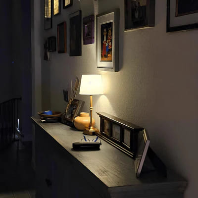 AMBIENTIFY Classic cordless table lamp with fabric shade and iron stem, casting warm ambient light on a bedside table. Three brightness settings and up to 40 hours battery life. Suitable for bedroom, living room and home office.