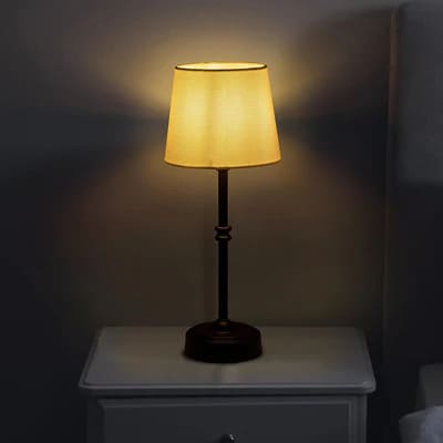 AMBIENTIFY Classic cordless table lamp with fabric shade and iron stem, casting warm ambient light on a bedside table. Three brightness settings and up to 40 hours battery life. Suitable for bedroom, living room and home office.