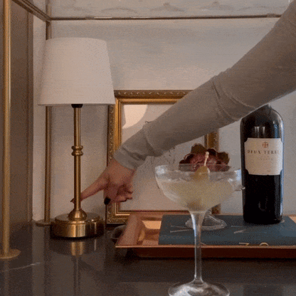AMBIENTIFY Classic cordless table lamp with fabric shade and iron stem, casting warm ambient light on a bedside table. Three brightness settings and up to 40 hours battery life. Suitable for bedroom, living room and home office.