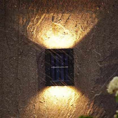 SOLARIFY One solar-powered outdoor wall light mounted on a stone wall, projecting warm white light upward and downward. IP65 weatherproof. Suitable for garden fences, façades, covered terraces and entrance walls.