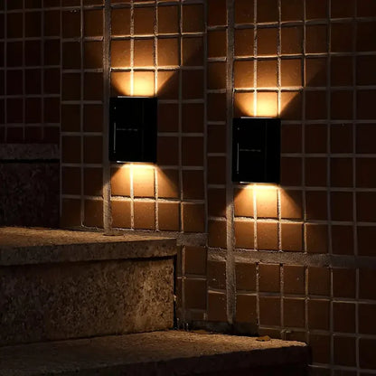 SOLARIFY One solar-powered outdoor wall light mounted on a stone wall, projecting warm white light upward and downward. IP65 weatherproof. Suitable for garden fences, façades, covered terraces and entrance walls.