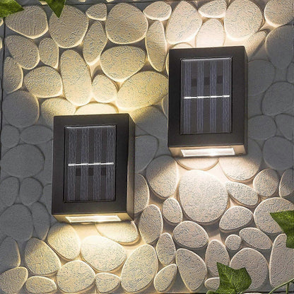 SOLARIFY One solar-powered outdoor wall light mounted on a stone wall, projecting warm white light upward and downward. IP65 weatherproof. Suitable for garden fences, façades, covered terraces and entrance walls.